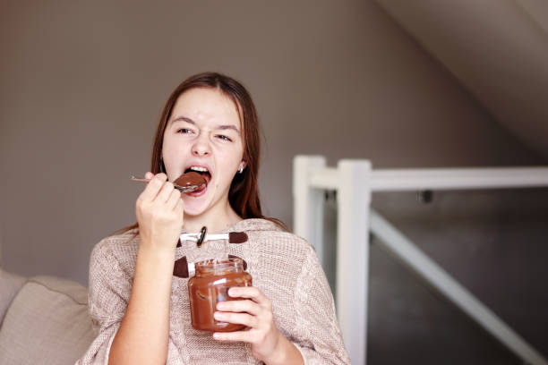 grappig tiener meisje genieten van het eten van chocolade cfream van glazen pot thuis. stop het dieet. geven van dieet. ongezond voedsel. - control room stockfoto's en -beelden