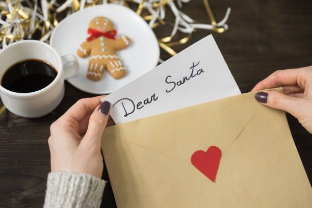 istock Female hands put a letter for Santa in an envelope. Gingerbread and coffee on background 1188085437