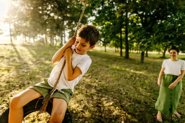 Photo of mother and son having fun in the nature, son is swinging on a tire swing