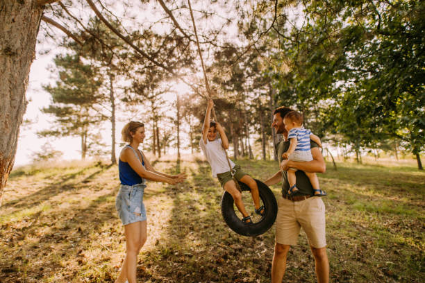 Family day in the nature Photo of a happy family having fun in the nature, boy is swinging on a tire swing tire swing stock pictures, royalty-free photos & images