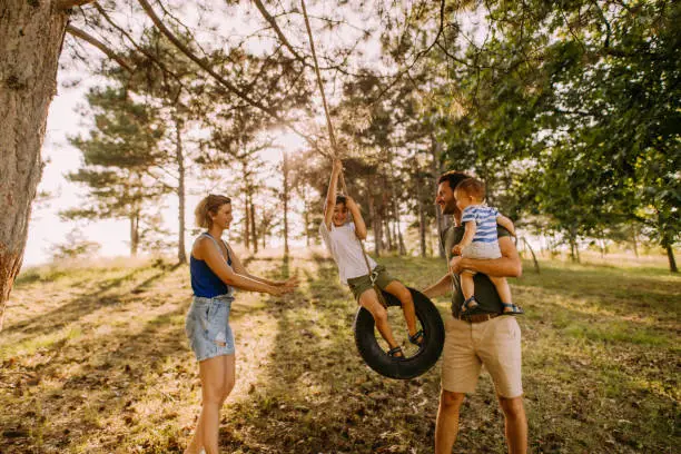 Photo of a happy family having fun in the nature, boy is swinging on a tire swing