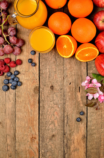 Orange juice, fresh oranges, apples, grapes, raspberries, blueberries and spring flowers on a wooden table - fruit background - view from above - vertical photo