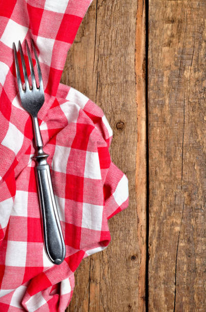 istock Fork on red checkered tablecloth right frame on vintage wooden table background - view from above - vertical photo 1188088974