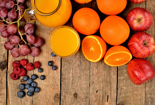 View from above of jug with orange juice, fresh oranges, apples, grapes, raspberries and blueberries on a wooden table - fruit background