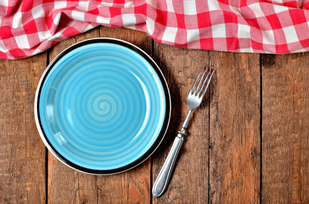 istock Blue ceramic plate, fork and red checkered tablecloth top frame on old vintage wooden table background - view from above 1188089061