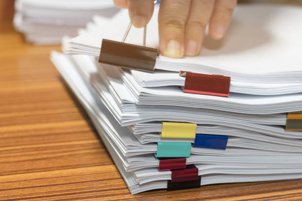 istock Teacher searching homework assignment stacked in archive with paperclips waiting to be managed and inspected. Pile of unfinished paperwork. Report papers stacks. Business and education concept. 1188144065