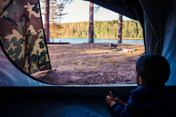 istock Little boy looking outside tent on lake landscape 1188147712