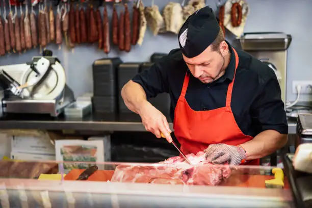 Male butcher boning fresh ham in a modern butcher shop with metal safety mesh glove