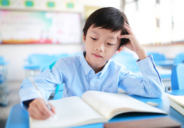istock Young boy reading at his desk in a classroom 1188160245
