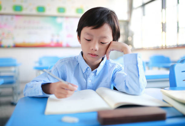 istock Young boy reading at his desk in a classroom 1188160761