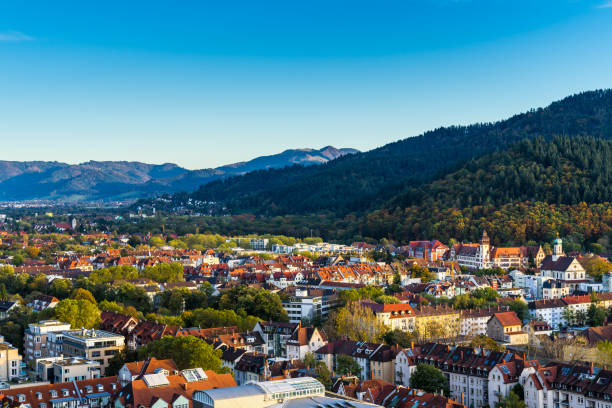 Germany, Aerial view above freiburg im breisgau city skyline and cityscape in valley surrounded by black forest mountains and nature landscape at sunset stock photo