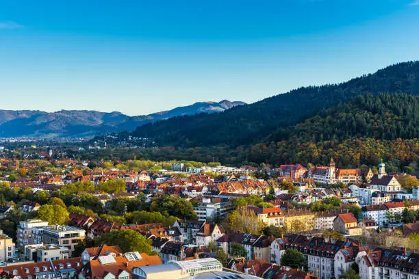 Germany, Aerial view above freiburg im breisgau city skyline and cityscape in valley surrounded by black forest mountains and nature landscape at sunset