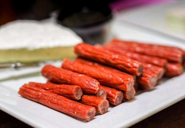 Preserved salami or meat sticks (red) in the foreground Preserved salami or meat sticks (red) in the foreground; block of cheese in the background. These are popular entertainment foods; sometimes called finger foods. Catering concept. prosciutto brie stock pictures, royalty-free photos & images