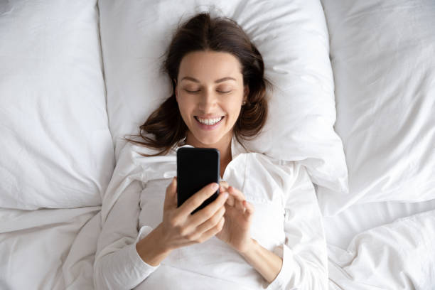 istock Happy young woman using phone lying in bed in morning 1188167162