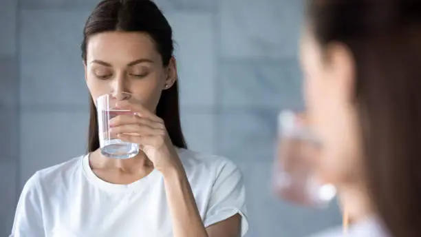 Photo of Attractive healthy young woman drink fresh mineral water in morning