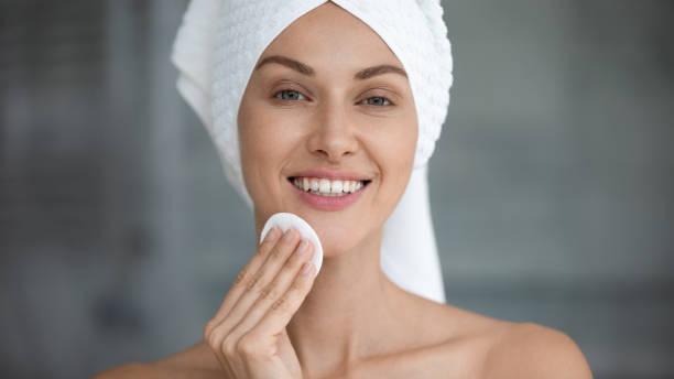 Smiling beautiful woman hold cotton pad cleansing face skin Smiling beautiful young woman with towel on head hold cotton pad disk cleansing face skin with cleanser, happy lady remove makeup look at camera enjoy healthy clean skincare beauty treatment concept tonic water stock pictures, royalty-free photos & images