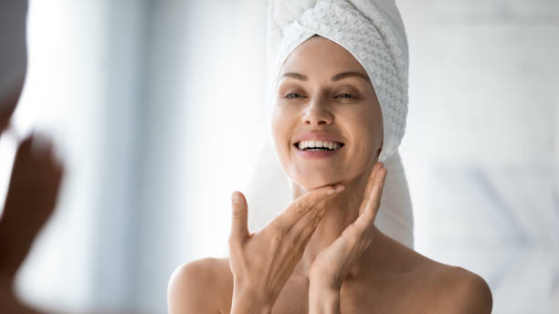 Happy lady look in bathroom mirror touching healthy face skin Happy confident young lady with towel on head look in bathroom mirror touching moisturized soft healthy sensitive skin doing morning hydration spa beauty routine, facial skincare treatment concept woman washing face stock pictures, royalty-free photos & images