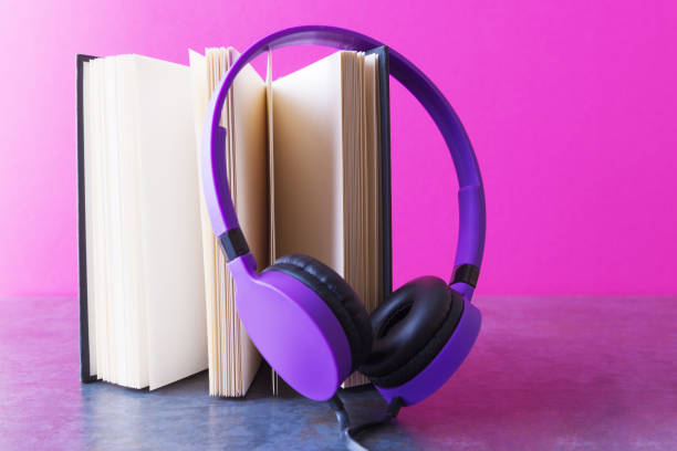 istock Open notebook with violet headphones over pink background. Audio book concept 1188173153