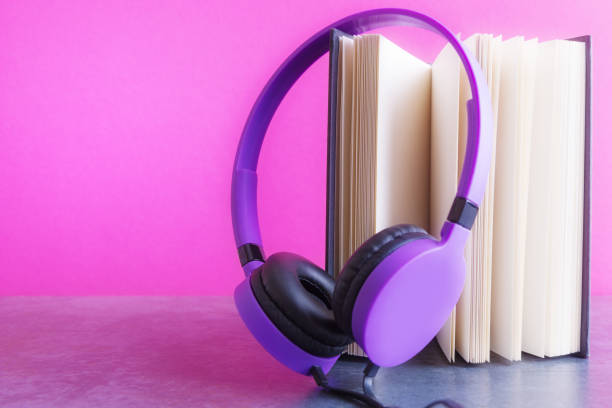istock Open notebook with violet headphones over pink background. Audio book concept 1188173183
