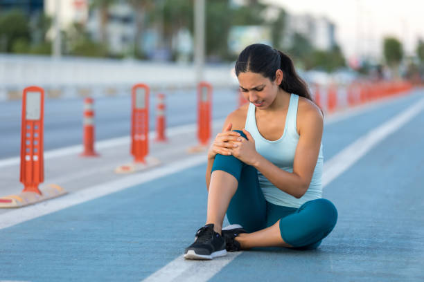 Female runner clutching injured knee Female runner clutching injured knee human knee stock pictures, royalty-free photos & images