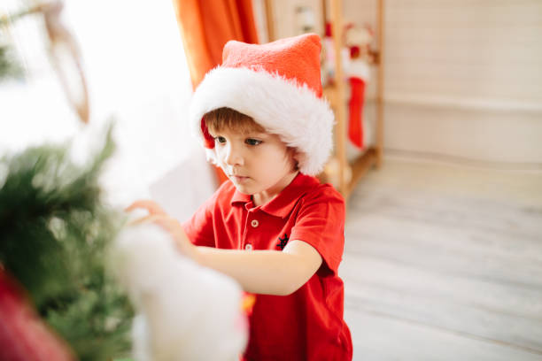 Cute little boy of about five year with blue eyes decorating a Christmas tree.