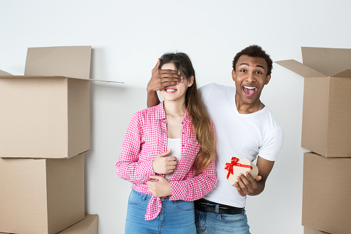 Happy young couple in a new apartment. Man giving surprise gift to woman against unpacked boxes.
