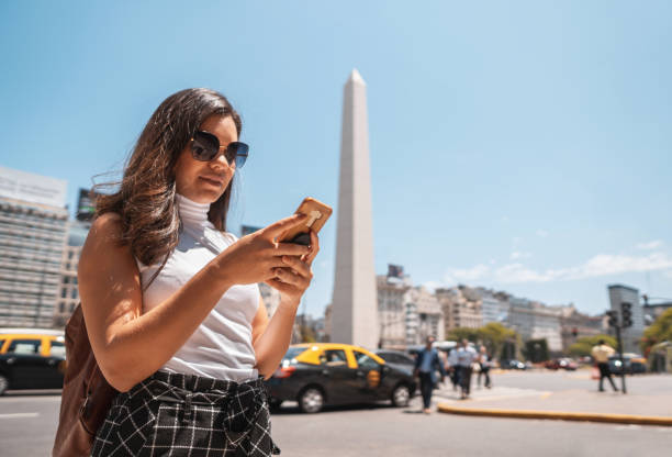 Woman using mobile phone in front of Obelisco de Buenos Aires Tourist crossing the crosswalk and using phone on the streets of Caba in Buenos Aires, Argentina argentinian culture stock pictures, royalty-free photos & images