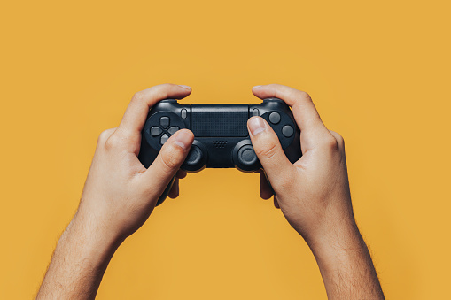 man gamer hands holding black gamepad on yellow background.