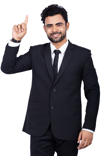 Portrait of confident Indian businessman pointing up. Handsome male professional is standing on white background. He is wearing elegant suit.