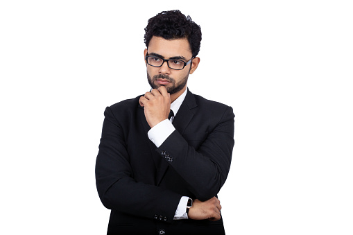 Indian businessman wearing glasses while thinking something. Handsome male professional is standing on white background. He is wearing elegant suit.