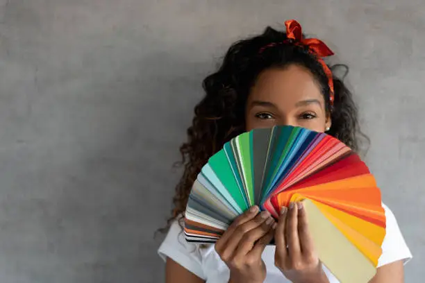 Happy African American woman painting her house and holding a color palette covering her face