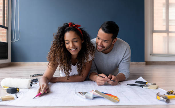 Loving couple looking at the blueprints of their new house Happy loving couple looking at the blueprints of their new house while lying on the floor smiling home improvement stock pictures, royalty-free photos & images