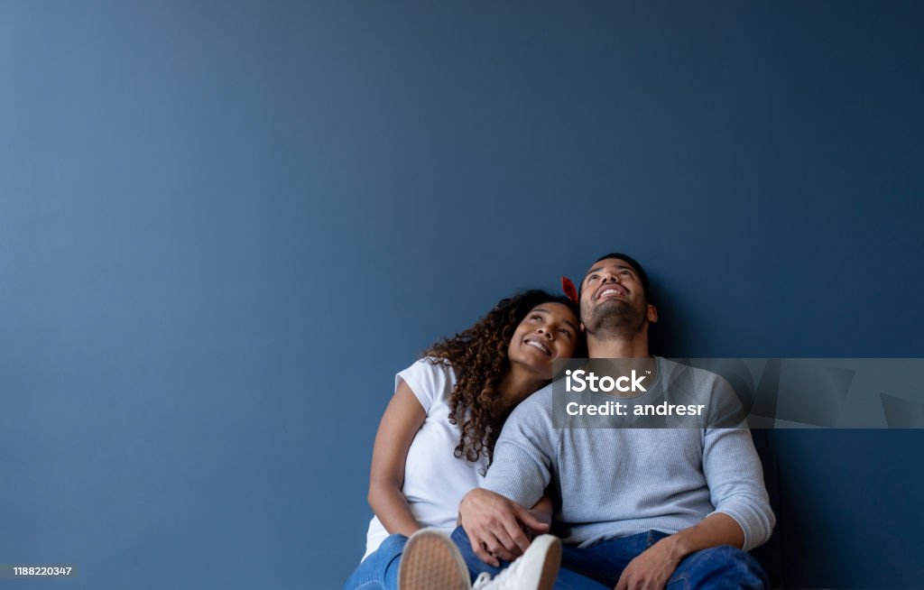 Thoughtful couple at home leaning against a wall and smiling Thoughtful couple at home leaning against a wall and smiling - real estate concepts Couple - Relationship Stock Photo