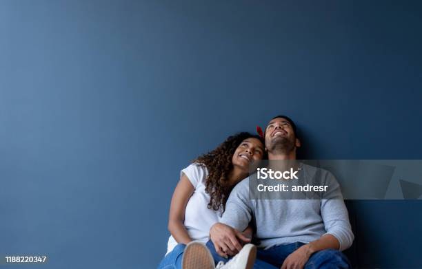 Thoughtful Couple At Home Leaning Against A Wall And Smiling Stock Photo - Download Image Now