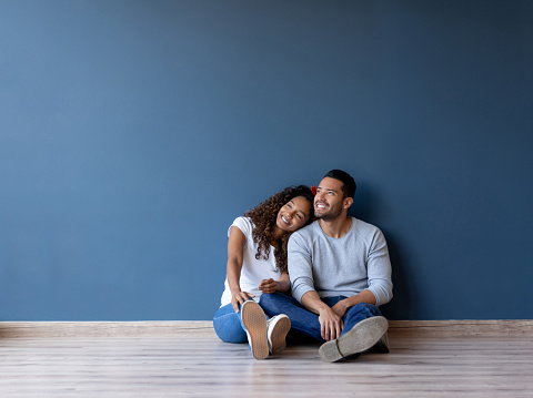 Happy couple smiling and sitting on the floor in their new home - real estate concepts