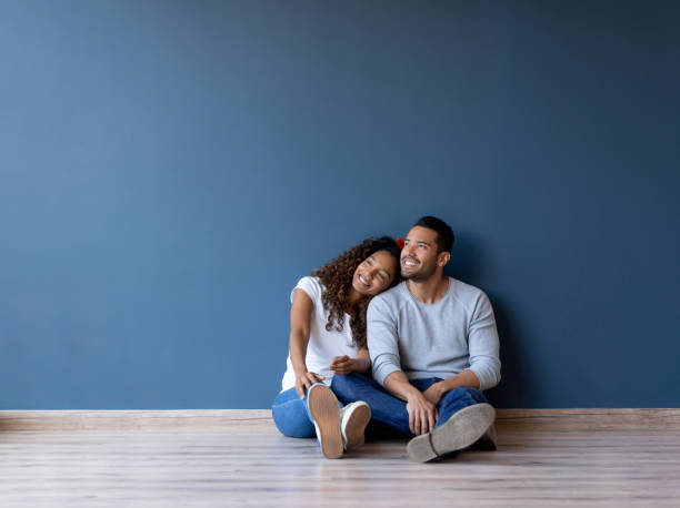 Happy couple smiling in their new home Happy couple smiling and sitting on the floor in their new home - real estate concepts new home stock pictures, royalty-free photos & images