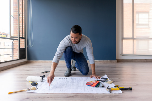 Happy Latin American man remodeling his house and drawing on a blueprint