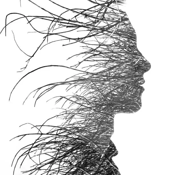 Photo of Double exposure of a young handsome man's profile portrait blended with many branches dissolving into his face, black and white