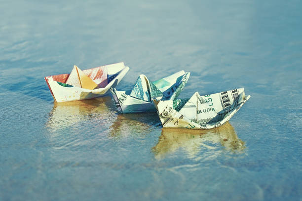 A boat made of paper money A boat made of paper money in sea sand A boat made from a dollar, euro, russian ruble at sea. Sea sand. The concept of money. making money origami stock pictures, royalty-free photos & images