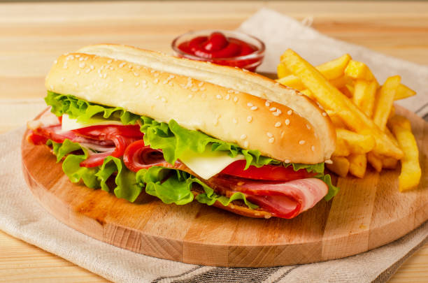 Submarine sandwich with bacon, cheese, tomatoes and lettuce on wooden background