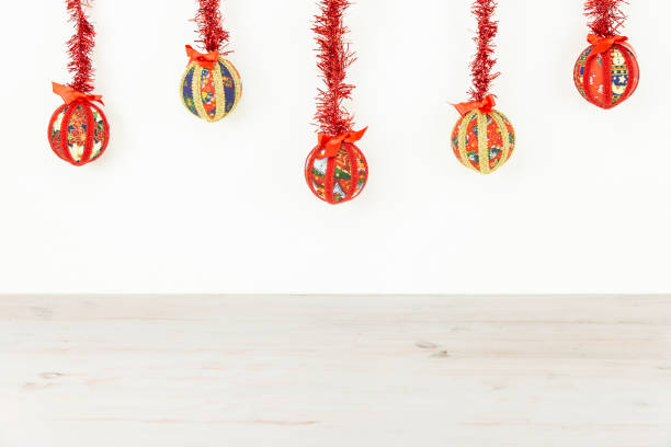 istock Christmas copy space: five Christmas baubles made by hand with the decoupage technique hung from top with a red shiny garland on white background and light wooden base on bottom 1188228938