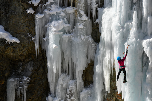 Pontresina, GR, Switzerland - February 22, 2019:\nIce climbing in the Bernina gorge near Pontresina.\nA young woman in a violet jacket and blue helmet climbs up the ice walls from below the Bernina gorge. In the canyon of Pontresina every winter huge ice walls with imposing icicles are created. Dedicated mountain guides work the rocks with water - so that an optimal ice density is formed and offers more variety to the climbers. The gorge is free for all ice climbing and free access. The picture was photographed by the main street, where you can watch the climbers well.\nPontresina is located at 1,805 meters in a side valley of Upper Engadin. Very close to the Bernina massif with the two most famous summits of the Engadine:\nPiz Palü and Piz Bernina. The latter counts with its 4'049 m as the highest peak of the Eastern Alps. Predestined peace can be found here\nas well as action and variety.