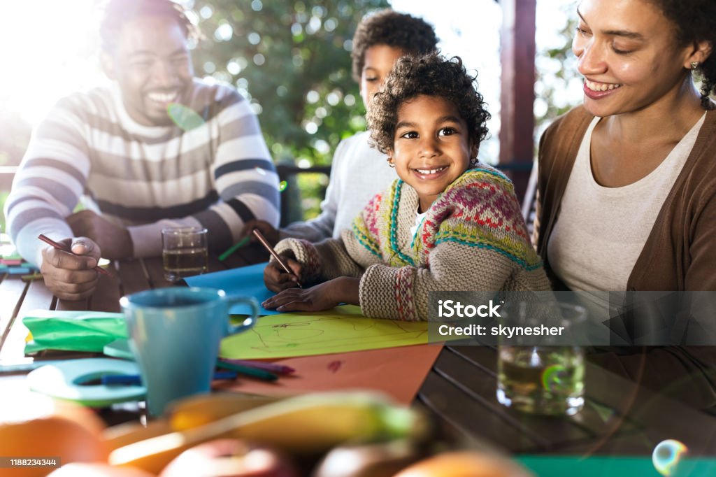 Happy black family enjoying while drawing together on a balcony. Young happy African American family coloring on a terrace. Focus is on girl. Adult Stock Photo