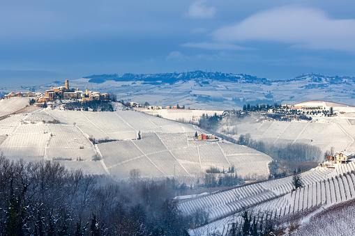 View of small medieval town and vineyards on the hills covered in snow in Piedmont, Northern Italy.