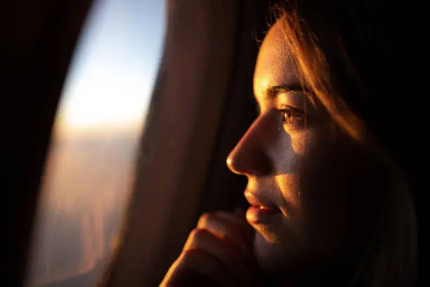 Photo of Close up of pensive woman looking at sunset through airplane window.