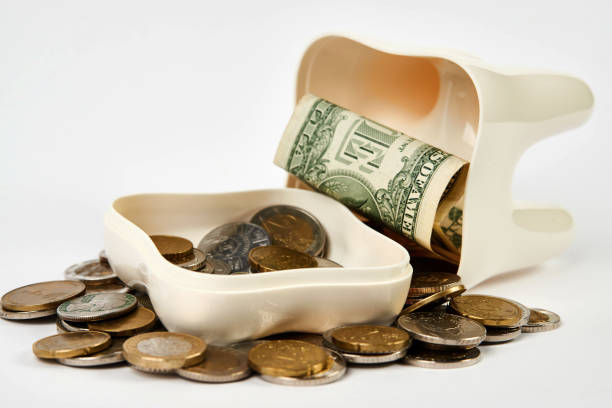Tooth piggy bank with coins on white background with copy space. Tooth and money close-up. Saving money for dental healthcare. Dentist Money, Medical treatment concept.