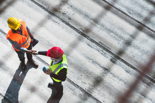 sobre la vista de la cabeza de dos arquitectos que se dan la mano en el sitio de construcción - hardhat construction men handshake fotografías e imágenes de stock