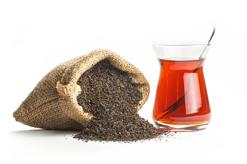 Glass Turkish brewed black tea and dry black tea in burlap sack isolated on white background. Turkish traditional hot drink