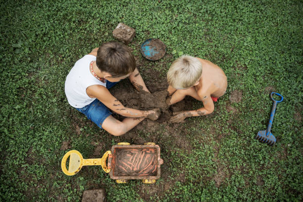 Top view of two brothers sitting on green grass playing with mud covering their legs in it.