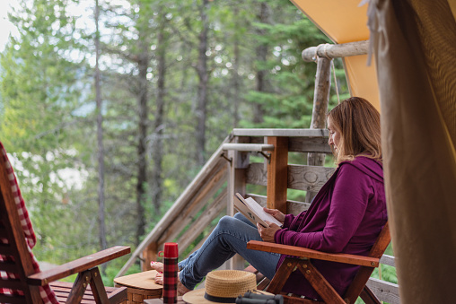woman relaxing with a book outside luxury tent in woods of Montana